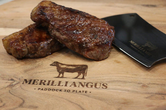 Cooked beef steaks on wooden board with cleaver, Merilli Angus paddock to plate logo